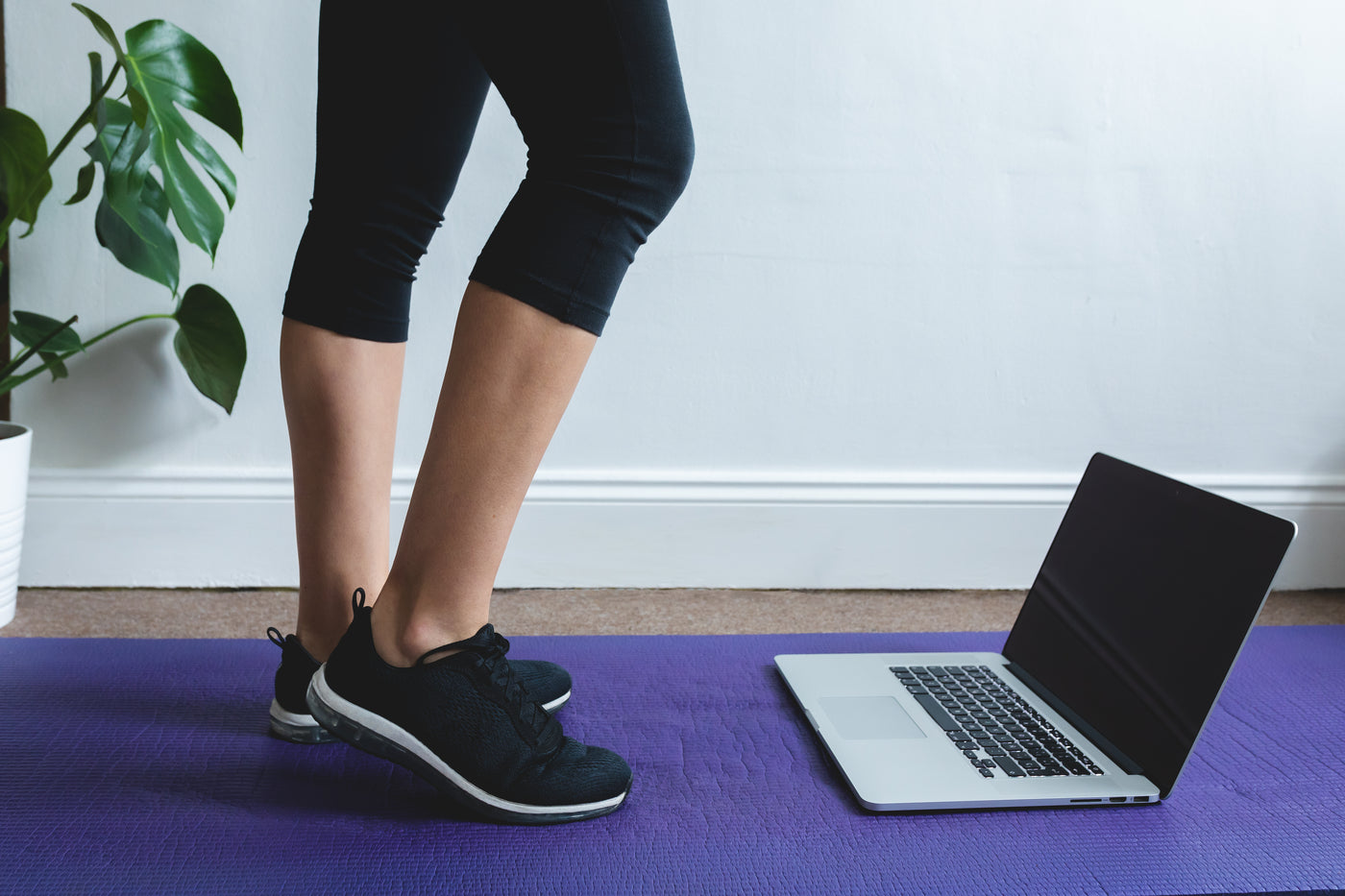 Ein aufgeklappter Laptop steht auf einer Yogamatte, daneben eine Person in Sportkleidung